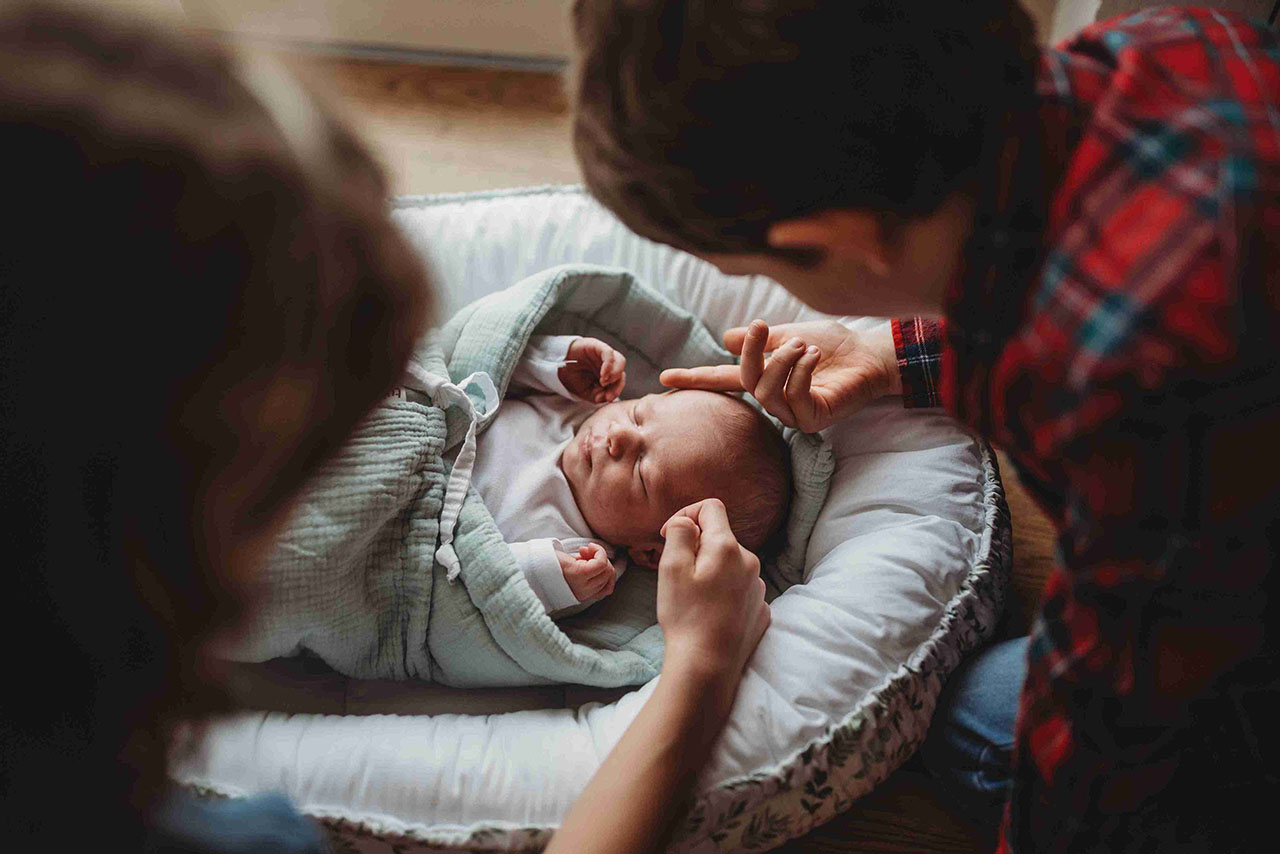 Klidné novorozeně pohodlně spící v měkkém šátku na nošení, držené rodičem.